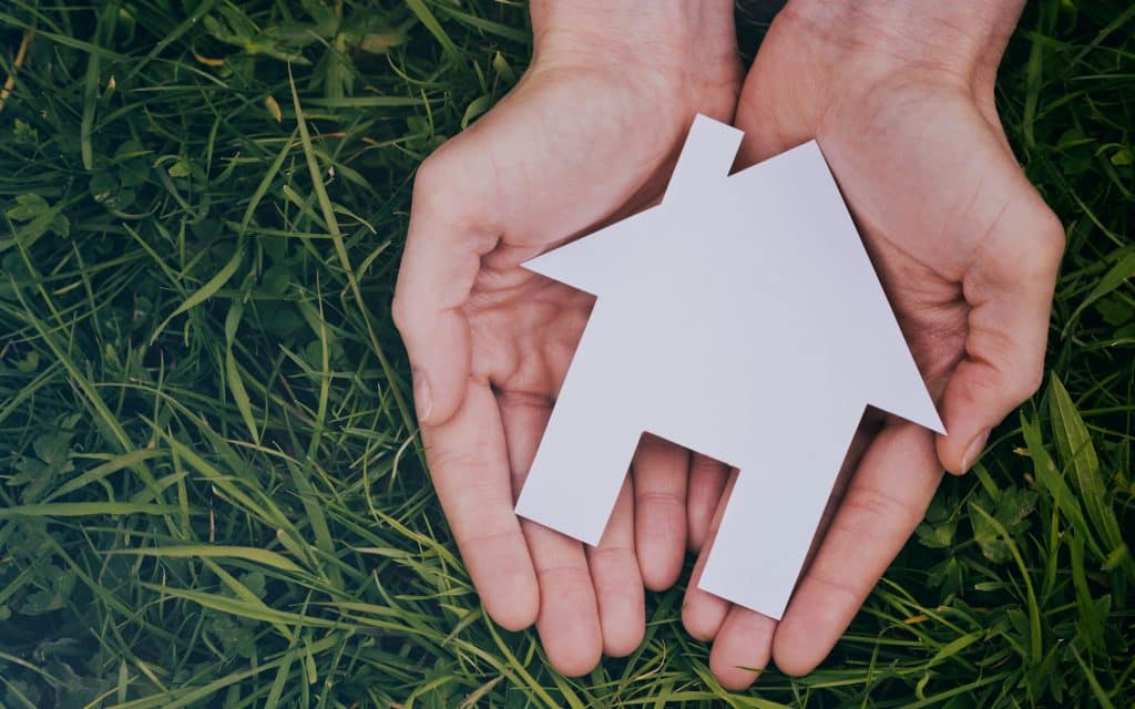 Hand holding a small white paper house, symbolizing home care, safety, and support for the elderly