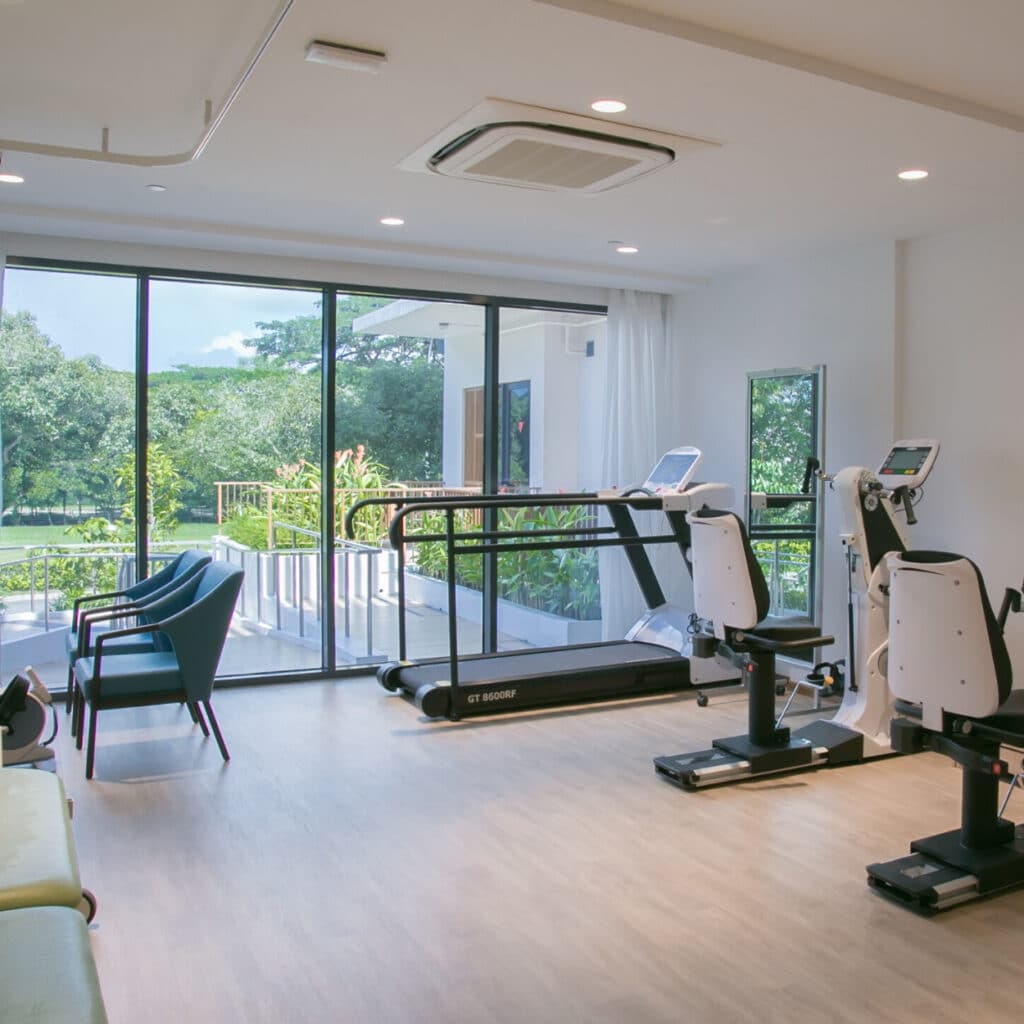 Resident using rehabilitation equipment in a bright wellness studio overlooking greenery
